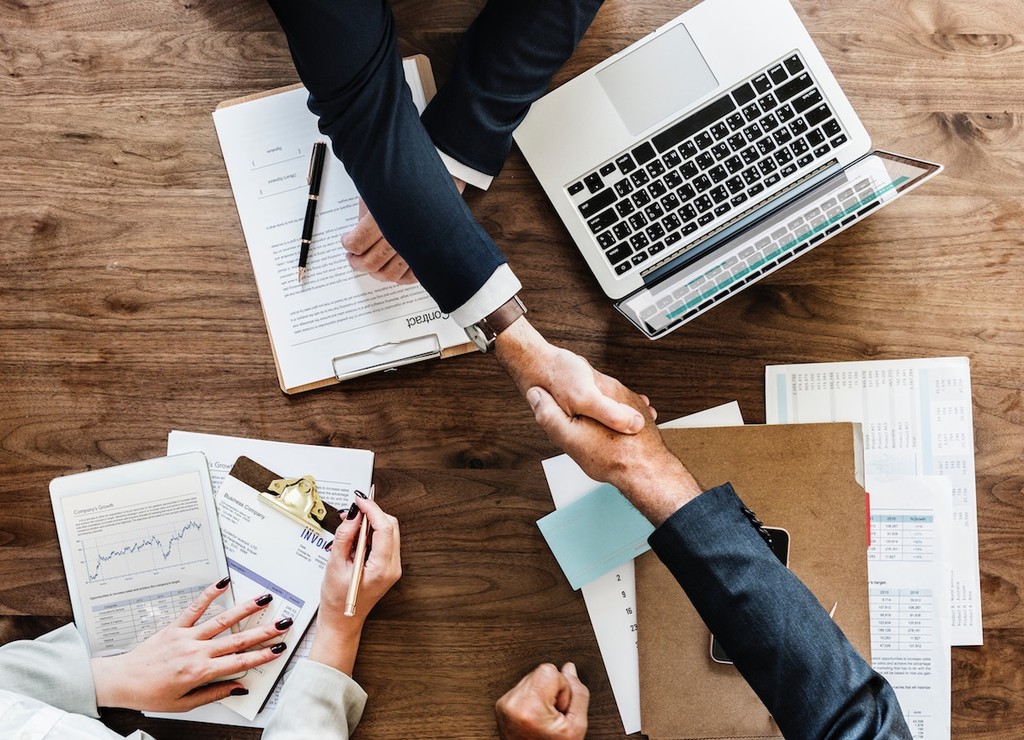 Two people shaking hands across a desk of printed reports